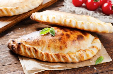 Lezzetli pizza Calzone, domatesli geleneksel İtalyan pizzası ve ahşap arka planda taze fesleğen.