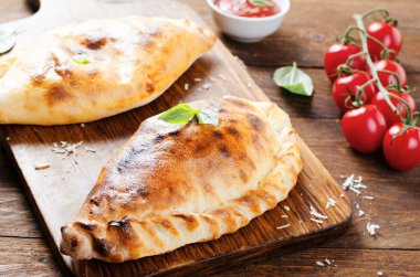 Lezzetli pizza Calzone, domatesli geleneksel İtalyan pizzası ve ahşap arka planda taze fesleğen.