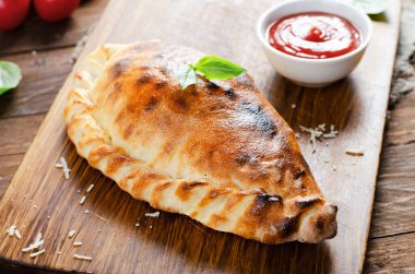 Lezzetli pizza Calzone, domatesli geleneksel İtalyan pizzası ve ahşap arka planda taze fesleğen.