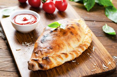 Lezzetli pizza Calzone, domatesli geleneksel İtalyan pizzası ve ahşap arka planda taze fesleğen.