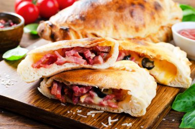 Lezzetli pizza Calzone, geleneksel İtalyan pizzası Jambonlu peynir domatesli ve ahşap arka planda taze fesleğen