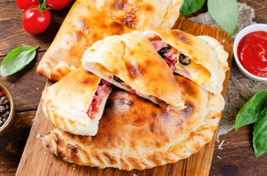 Lezzetli pizza Calzone, geleneksel İtalyan pizzası Jambonlu peynir domatesli ve ahşap arka planda taze fesleğen