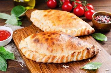 Lezzetli pizza Calzone, domatesli geleneksel İtalyan pizzası ve ahşap arka planda taze fesleğen.