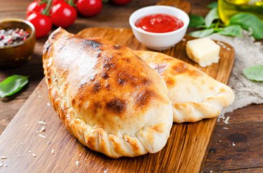 Lezzetli pizza Calzone, domatesli geleneksel İtalyan pizzası ve ahşap arka planda taze fesleğen.