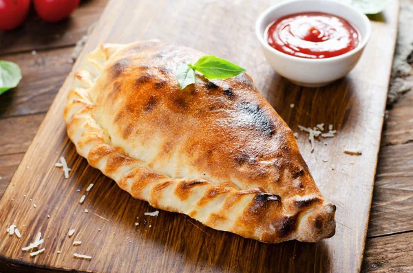 Lezzetli pizza Calzone, domatesli geleneksel İtalyan pizzası ve ahşap arka planda taze fesleğen.