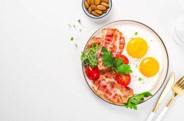 Kızarmış yumurta ve pastırma ile vişneli domates tabakta, kahvaltıda, Keto 'da, Paleo diyetinde parlak arka planda.
