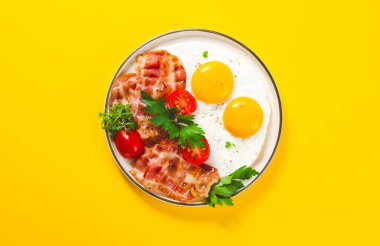 Kızarmış yumurta ve pastırma ile vişneli domates tabakta, kahvaltıda, Keto 'da, Paleo diyetinde, sarı arka planda.