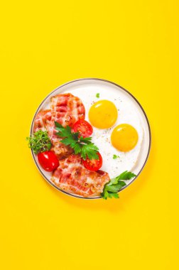 Kızarmış yumurta ve pastırma ile vişneli domates tabakta, kahvaltıda, Keto 'da, Paleo diyetinde, sarı arka planda.