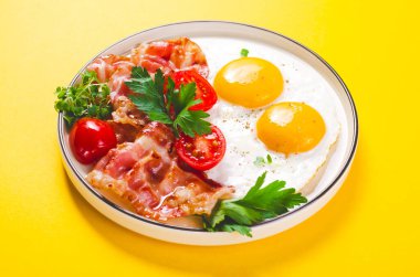 Kızarmış yumurta ve pastırma ile vişneli domates tabakta, kahvaltıda, Keto 'da, Paleo diyetinde, sarı arka planda.