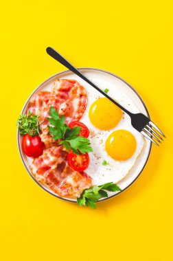 Kızarmış yumurta ve pastırma ile vişneli domates tabakta, kahvaltıda, Keto 'da, Paleo diyetinde, sarı arka planda.