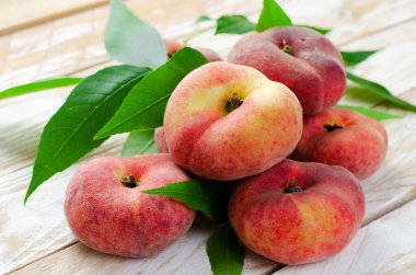 Taze Düz Şeftaliler, Çin Satürn Donut Şeftalileri ve Parlak Arkaplanda Yapraklar