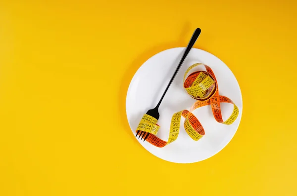ダイエット 重量損失の概念 測定テープと黄色の背景上のフォークと空のプレート — ストック写真