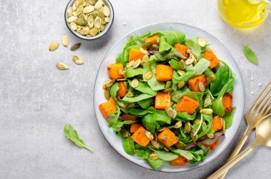 Arugula ve Balkabağı tohumlu balkabağı salatası, Kızarmış balkabağı salatası, Beton Arka planda Taze Vegan Sonbahar Salatası