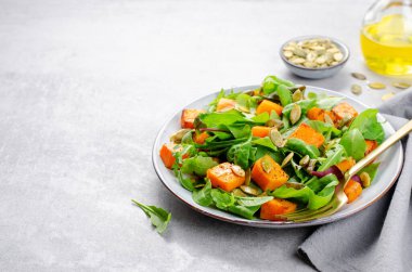 Arugula ve Balkabağı tohumlu balkabağı salatası, Kızarmış balkabağı salatası, Beton Arka planda Taze Vegan Sonbahar Salatası