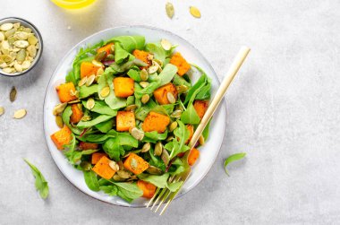 Arugula ve Balkabağı tohumlu balkabağı salatası, Kızarmış balkabağı salatası, Beton Arka planda Taze Vegan Sonbahar Salatası
