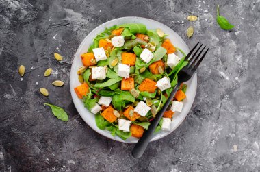 Arugula, Feta peyniri ve balkabağı tohumlu balkabağı salatası, kavrulmuş balkabağı salatası, karanlık arka planda sonbahar salatası.