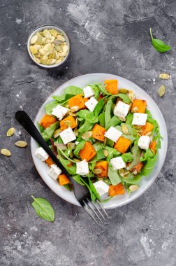 Arugula, Feta peyniri ve balkabağı tohumlu balkabağı salatası, kavrulmuş balkabağı salatası, karanlık arka planda sonbahar salatası.