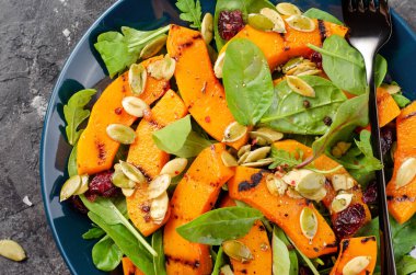 Arugula, ıspanak ve balkabağı tohumlu ızgara balkabağı salatası, kavrulmuş balkabağı salatası, arka planda sonbahar salatası.