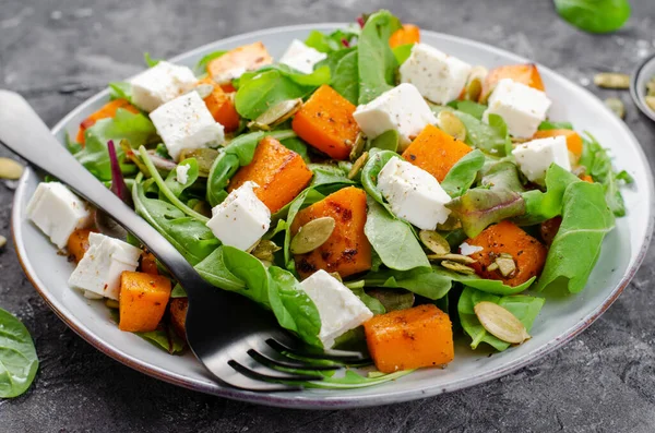 Arugula, Feta peyniri ve balkabağı tohumlu balkabağı salatası, kavrulmuş balkabağı salatası, karanlık arka planda sonbahar salatası.