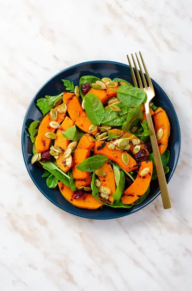 Grilled Pumpkin Salad with Arugula, Spinach, and Pumpkin Seeds, Salad Mix with Roasted Pumpkin, Autumn Salad on Bright Background