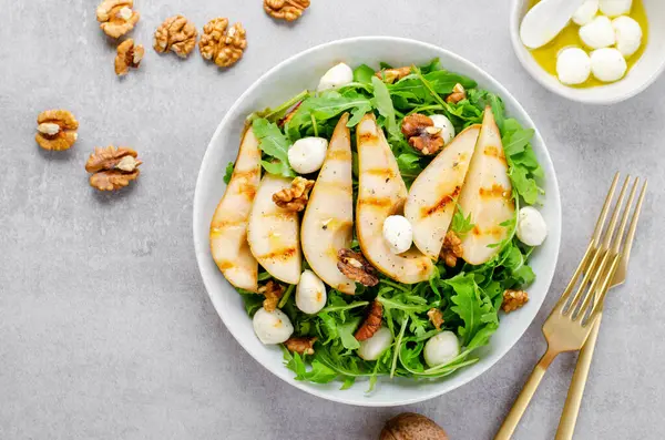 Izgara Armut Salatası, Armut, Arugula, Mozzarella İncileri, Ceviz ve Parlak Arkaplanda Giyinme Üzerine Taze Salata