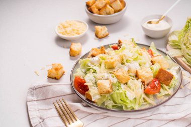 Marul, peynir, vişneli domates, kızarmış ekmek ve tabakta sos ile Sezar Salatası.