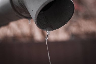 Su, kanalizasyon borusundan sarkık bir buzdan aşağı akıyor.