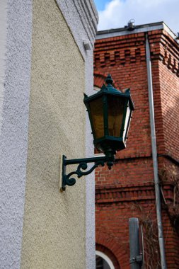 Alçılı bir binanın ön cephesinde metal bir desteğe sahip klasik sokak feneri ve arka planında tuğla mimarisi var..