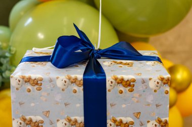 Arkaplanda mavi kurdele ve yeşil balonlar olan hediye kutusu. Bir çocuk için hediye paketi.