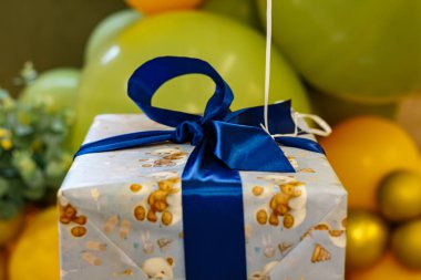 Arkaplanda mavi kurdele ve yeşil balonlar olan hediye kutusu. Bir çocuk için hediye paketi.