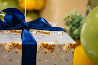Arkaplanda mavi kurdele ve yeşil balonlar olan hediye kutusu. Bir çocuk için hediye paketi.