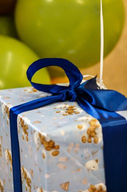 Arkaplanda mavi kurdele ve yeşil balonlar olan hediye kutusu. Bir çocuk için hediye paketi.