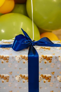 Arkaplanda mavi kurdele ve yeşil balonlar olan hediye kutusu. Bir çocuk için hediye paketi.
