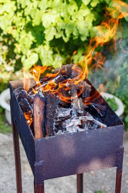 Parlak alevleri ve parlayan kömürleri olan metal bir ızgarada odun yakmak, yaz bahçesinde yakın çekim yapmak, barbekü ve açık hava yemekleri kavramı.