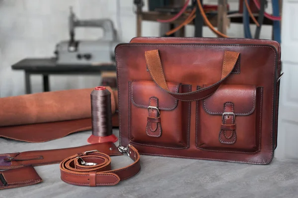 Retro leather men's bag made of genuine leather. The photo was created in a craft workshop. In the background are work tools and a belt. Brown leather briefcase. Satchel for work.