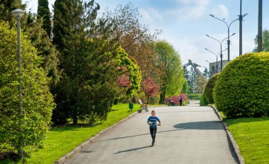 TERNOPIL, UKRAINE - 09 Mayıs 2020 - güzel sokaklar ve küçük çocuk bahar zamanı parkta scooter 'a biniyor. Ternopil 'deki Rönesans Parkı