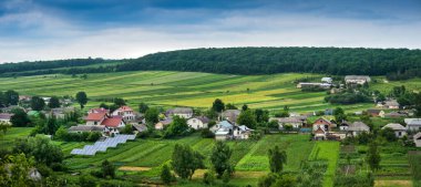 Bahçedeki güneş panellerinin panoramik üst görüntüsü, evler, araziler ve tarım arazileri, ufukta bulutlu doğal manzara