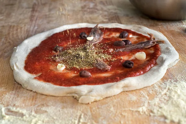 Traditional Neapolitan pizza with tomato sauce, anchovies, black olives, process of making pizzaiola from fermented dough with flour on the table