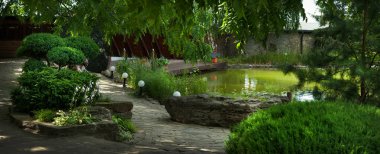 Bahçenin rahat bir köşesi, bir gölet ve çeşitli çalılar ve ağaçlar, manzara tasarımı.