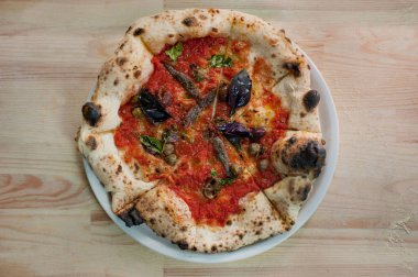 Domates soslu pizza, fesleğen, kapari, ançüez, yakın plan masada zeytin, ahşap fırından ev yapımı İtalyan hamuru.