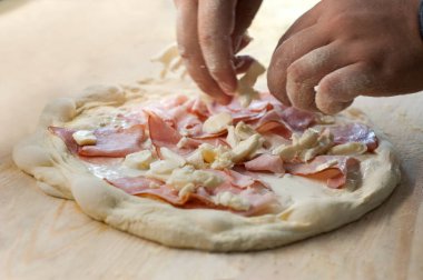 Şefin elleri pizza hamuruna jambon ve peynir koyuyor.
