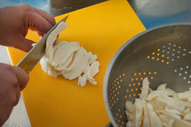 Aşçı kevgir peynirinin içeriği için bir tahta dilimler halinde bufalo peyniri keser.