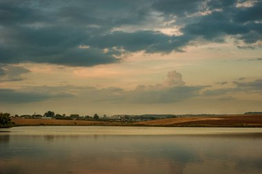 Sakin bir göletin güzel manzarası ve akşam gökyüzü, karşı kıyıdaki tarlaların manzarası, akşam geç saatlerde.