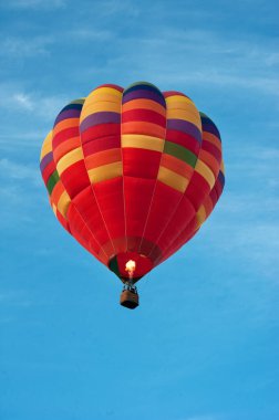 Mavi gökyüzünde sepeti olan çok renkli parlak balon. Ateş kubbedeki havayı ısıtır.
