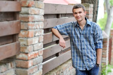 Kareli gömlekli bir gencin portresi eski moda bir çitin yanında duruyor.