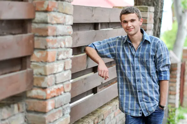 Kareli gömlekli bir gencin portresi eski moda bir çitin yanında duruyor.