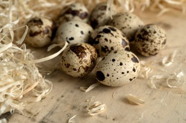 Benekli bıldırcın yumurtalarıyla yaşam, ahşap bir yüzeye yakın, dekoratif samanla çevrili.