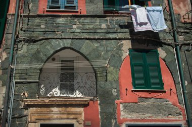 Monterosso al Mare 'deki eski bir evin ön cephesinde ortaçağ taşı ve kırmızı alçıdan yapılmış kemerli detaylar, balkonda kepenkler ve çarşaflar, İtalya' nın rengi.