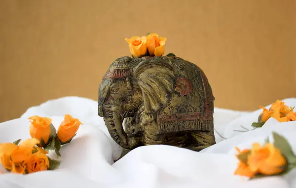 Beyaz kumaş üzerine antik Hint fil heykeli ve turuncu renkli çiçekler. Kopya için yeri var.