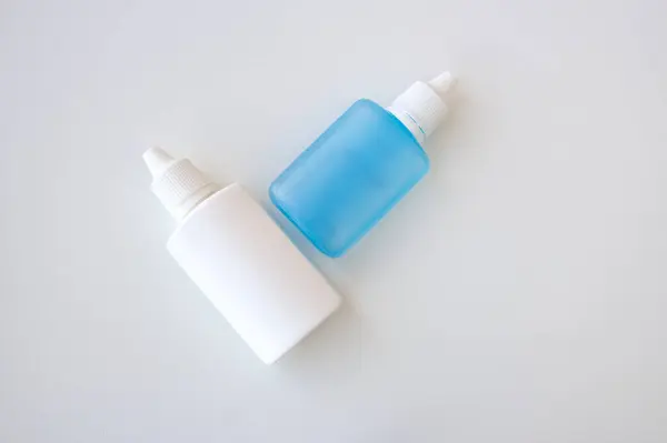 Beyaz arka planda iki tıbbi sıkıştırılabilir plastik şişe ve kopyası için yer var. Beyaz ve mavi göz damlaları.